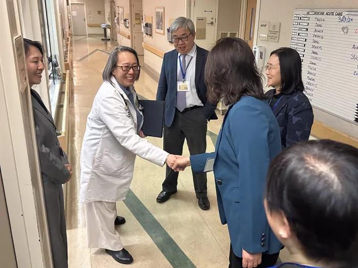 Woman in a white lab coat shaking hands of someone wearing a blue blazer