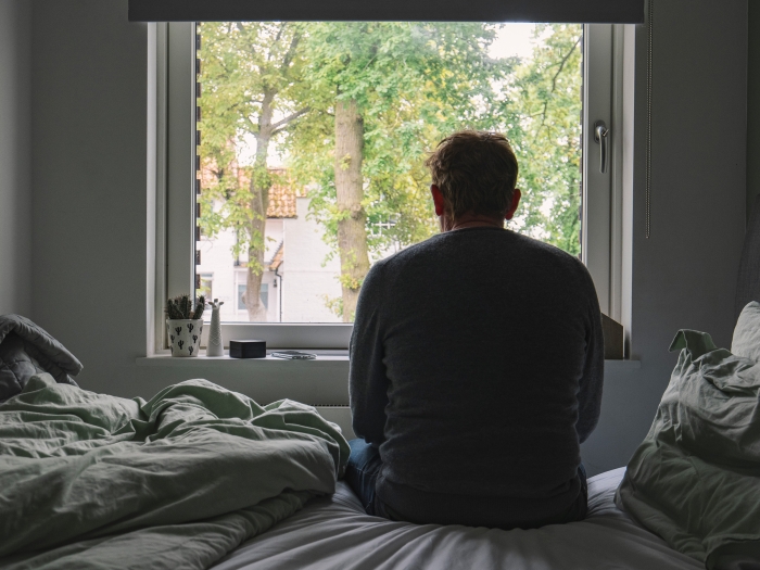 Man looking out window of bedroom. 