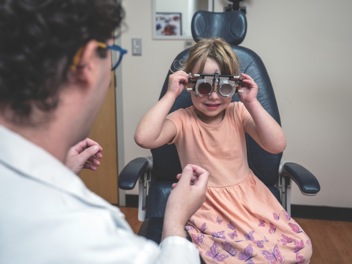 A little girl wearing a peach-colored dress is holding a pair of glasses used in a vision exam.