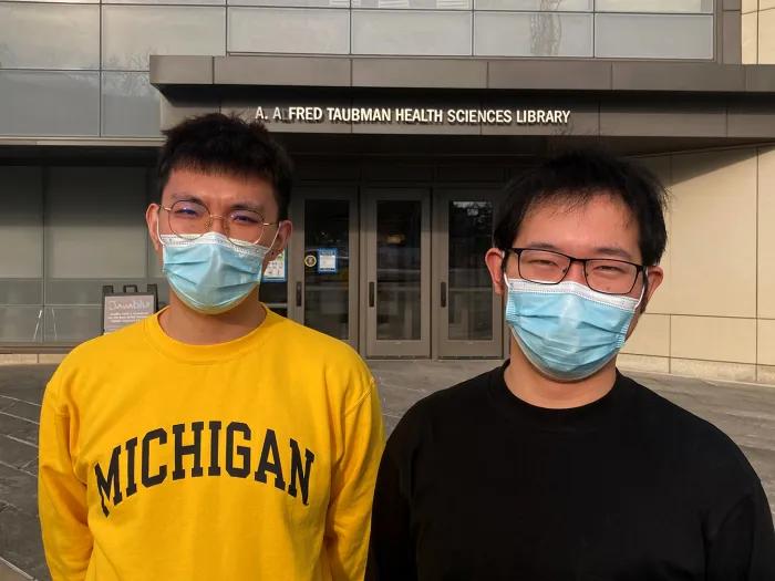 Two men wearing glasses and surgical masks standing in front of the A. Alfred Taubman Health Sciences Library