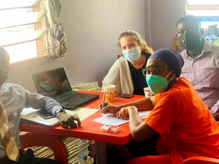 Four people wearing face masks sitting around a small orange table