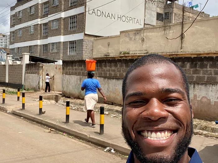 Man smiling and standing on the street in front of a sidewalk and building
