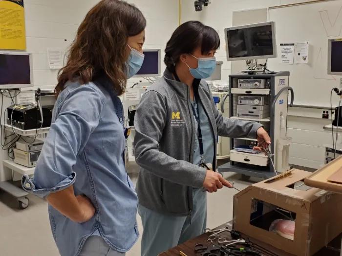 Two people wearing surgical masks looking at a scientific instrument made out of a cardboard box