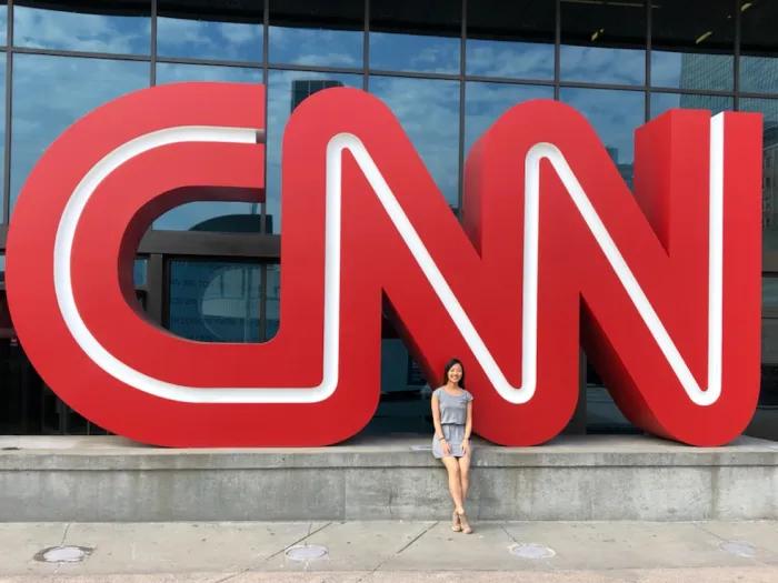 A large statue of the CNN logo in front of a building, with a woman standing in front of the logo