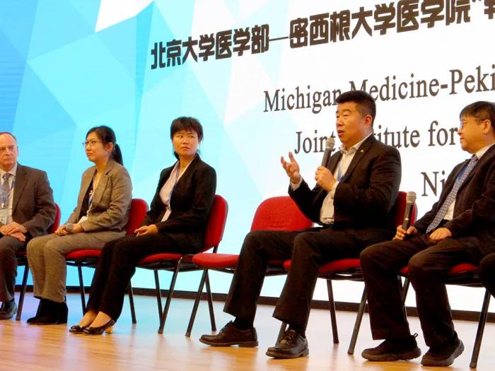 Five people in business attire sitting on chairs on a stage.