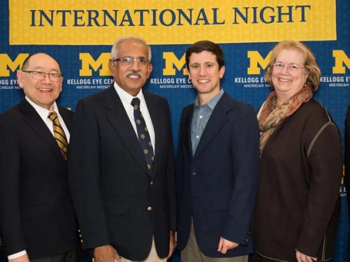 Six people standing in front of a Michigan sign backdrop that reads 'International Night'