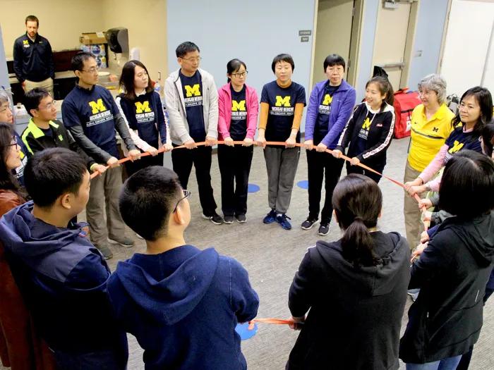 Group of people standing in a circle, all holding a long piece of cloth that forms the circle shape 