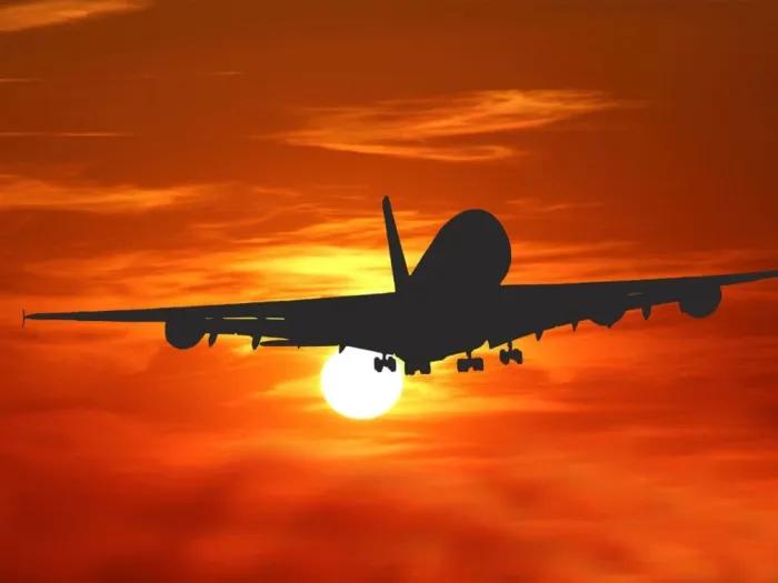 Silhouette of an airplane flying towards the sun, against the backdrop of a deep orange sunset