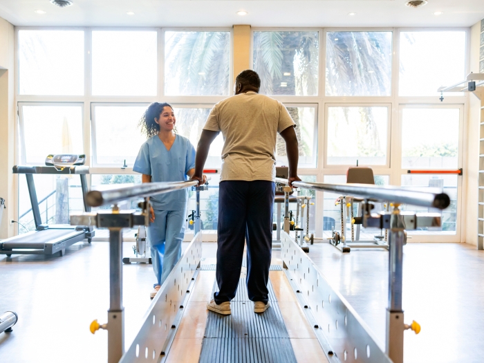 man walking on treadmill in open space with person in blue scrubs and scrub hat