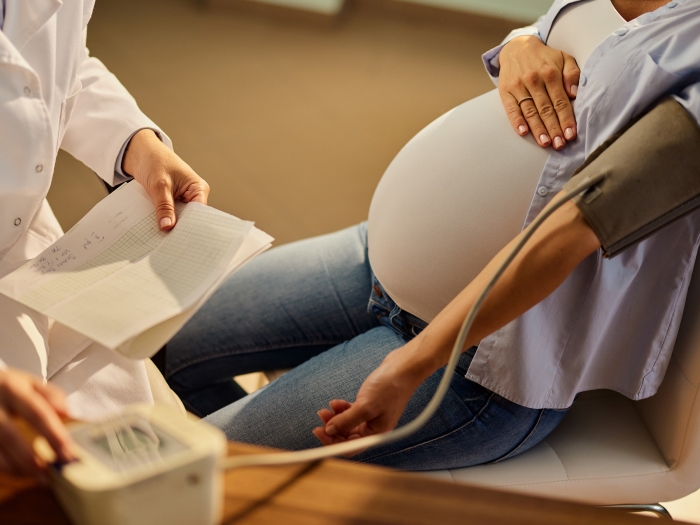 woman pregnant laying back with doctor looking at paper work and her getting blood pressure measured