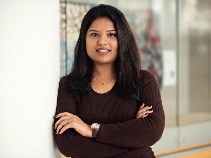 Hitarthi Vyas leaning against a wall with her arms folded in a professional manner