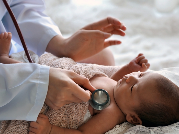 baby laying down with stethoscope over chest doctors hands