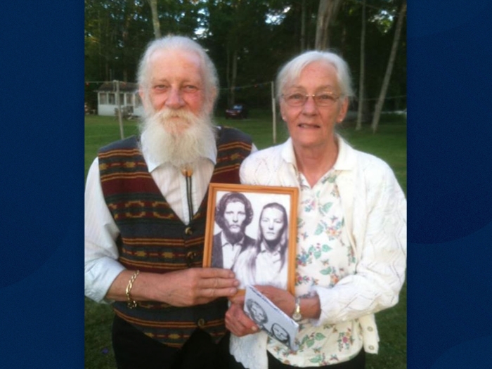 couple holding old photo of themselves in black and white in same position