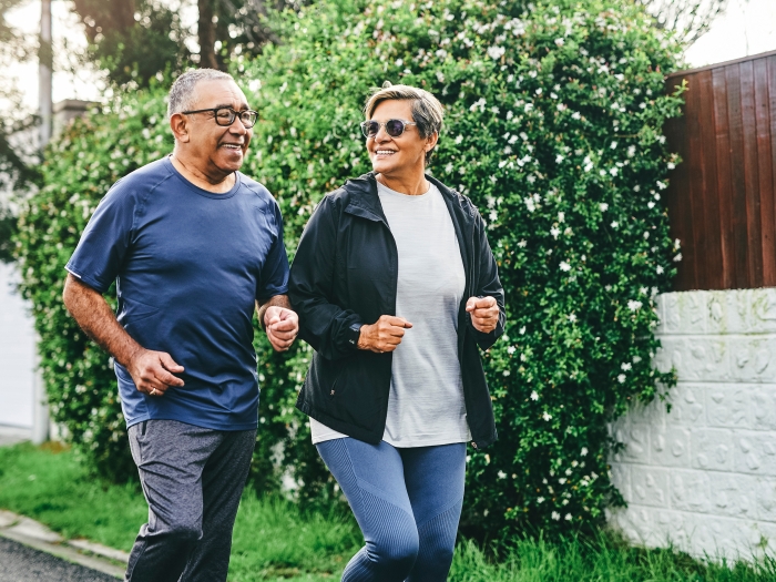 man and woman jogging outside with greenery behind them and fence on sidewalk