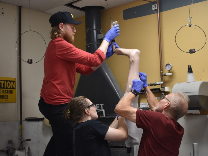 group working together on leg prosthetic in work room, one on top by foot and the other two on the calf of leg