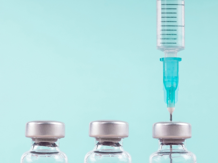 syringes three in a row with one with a shot going into it on a light teal background