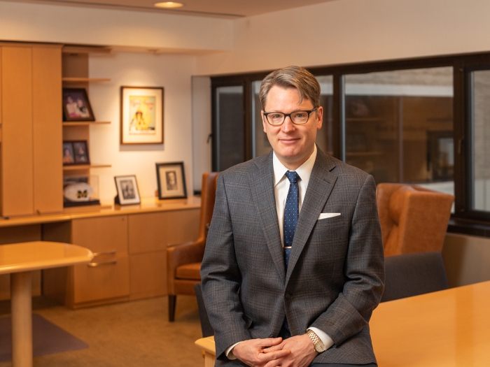 Smiling male doctor wearing glasses and a dark grey suit.