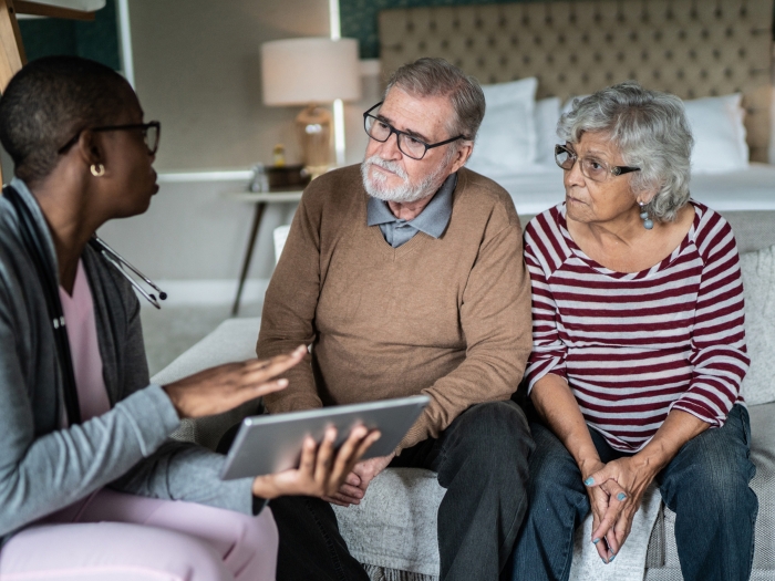 person talking to older couple on couch in living room