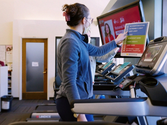 woman walking on treadmill picking intensity on a chart that reads from easier to harder