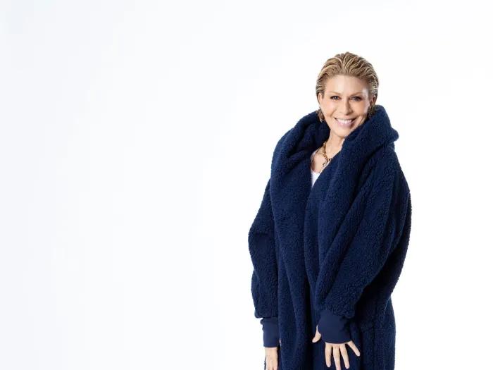 Smiling photo of Jill Martin. She is standing in a white space wearing a dark plush coat, jeans, and sneakers.
