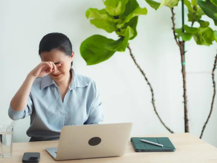 woman sitting by laptop putting hands on eyes