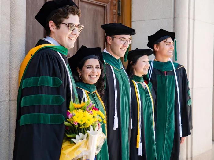 Five graduates stand in profile with one facing the camera