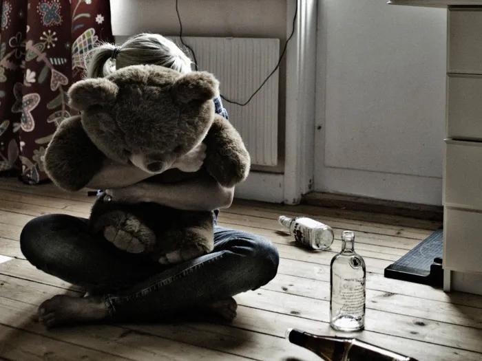 girl hugging teddy bear with alcohol bottles on ground