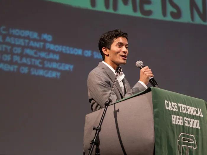 Medical student Mahesh stands at a lectern speaking at Cass Technical High School
