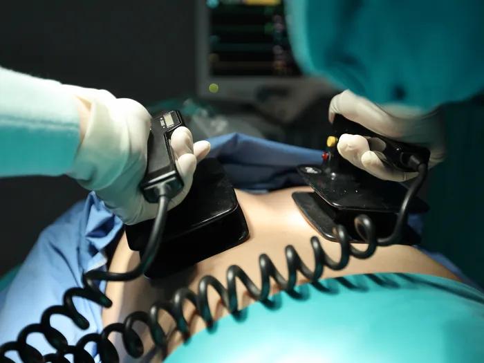 Close-up of clinician using defibrillator on patient in hospital