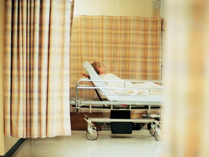 man in hospital bed through curtains that are off orange beige