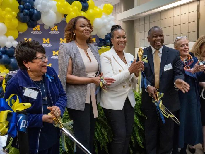 A group of people stand on a stage with balloons in the back. They are smiling and celebrating. Dr. Ebony Parker-Featherstone is at the center. 