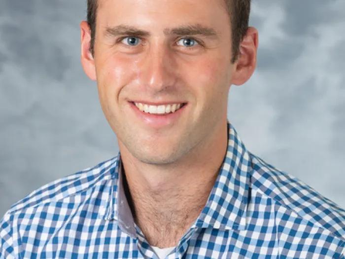 White male with dark hair, wearing a blue and white checked shirt.