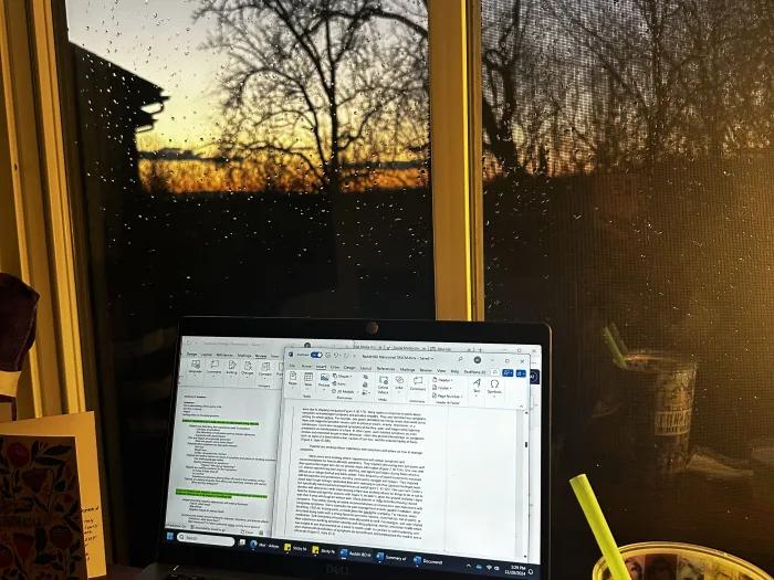 Image of an open laptop computer on a desk in front of a window with a sunset in the background