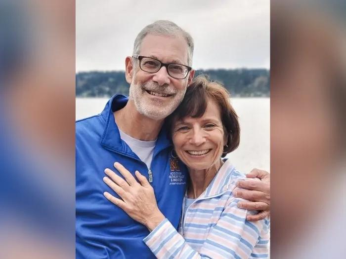Portrait of Sandy and Hassmiller standing together in front of a lake. They are smiling with their arms around each other affectionately.