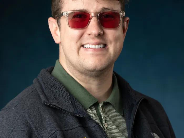 Man with dark hair and amber tinted glasses, wearing a dark grey Michigan Medicine sweater