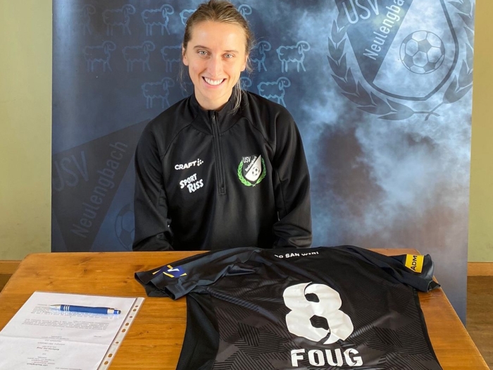 A woman sits at a table with a soccer jersey and signed contract
