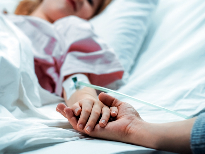 girl in hospital bed holding parents hand
