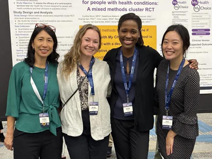 Group of women of diverse ages and races in front of a scientific poster
