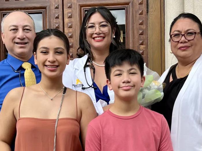 A family of five people: father, daughter in medical school white coat, mother, sister and brother