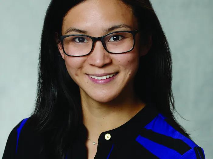 Woman of Asian descent with dark glasses, wearing a black and blue sweater