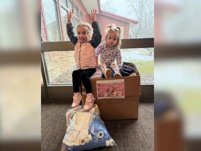 Two little girls sit on a box of donated blankets and towels for a humane society.