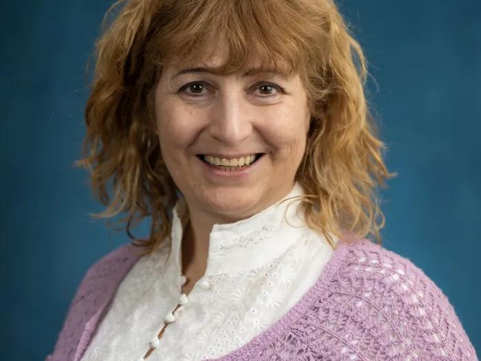 White woman with medium red hair, wearing a white blouse and lavender cardigan