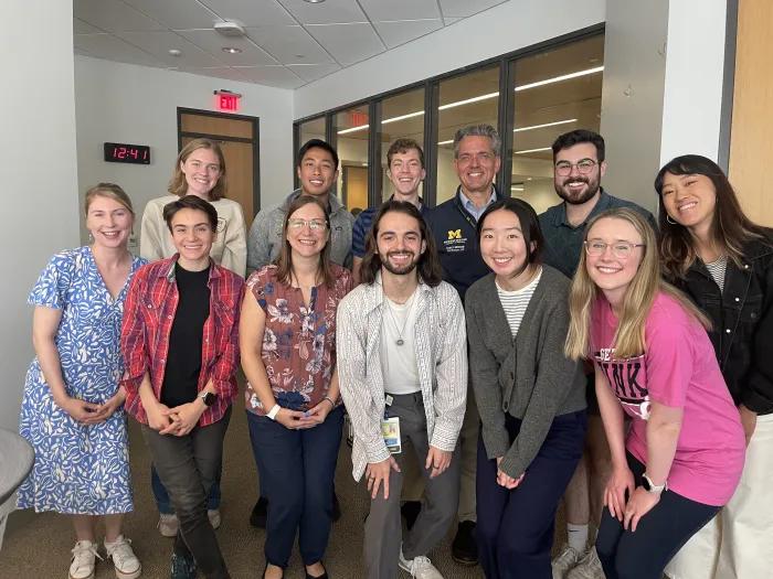 Group of 10 medical students and two faculty members, Beth Jones and Phil Rodgers, stand in two rows looking at the camera and smiling.