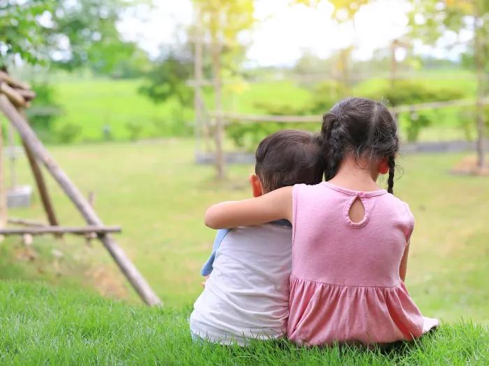 two little kids sitting in the grass with their backs to us