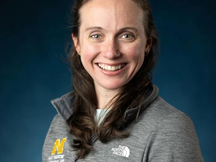 Woman with dark brown hair, wearing a grey pull-over U-M shirt.
