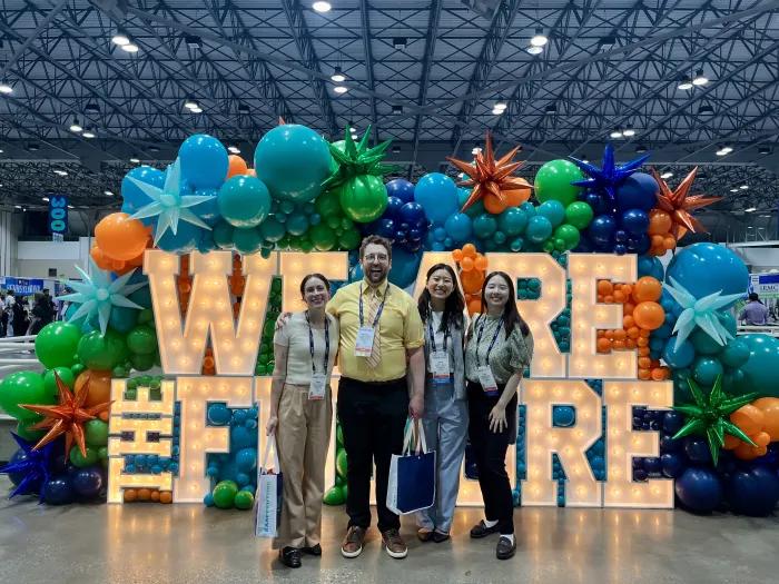 4 medical students stand in front a display with large, lighted letters that reads "We are the future" and colorful shaped balloons.