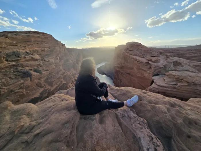 Woman sits with back facing to camera looking out over a sunny canyon 