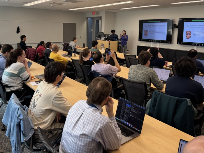 A classroom full of people at their laptops. Two people present at the front of the room.