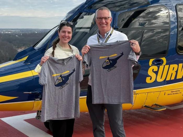 Two people pose with the new Tshirts in front of the U-M helicopters