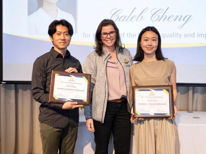 Two students holding certificates standing with a professor